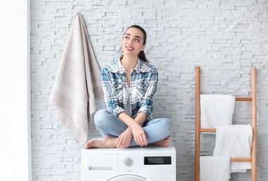 Photo of Young woman sitting on washing machine in laundry room