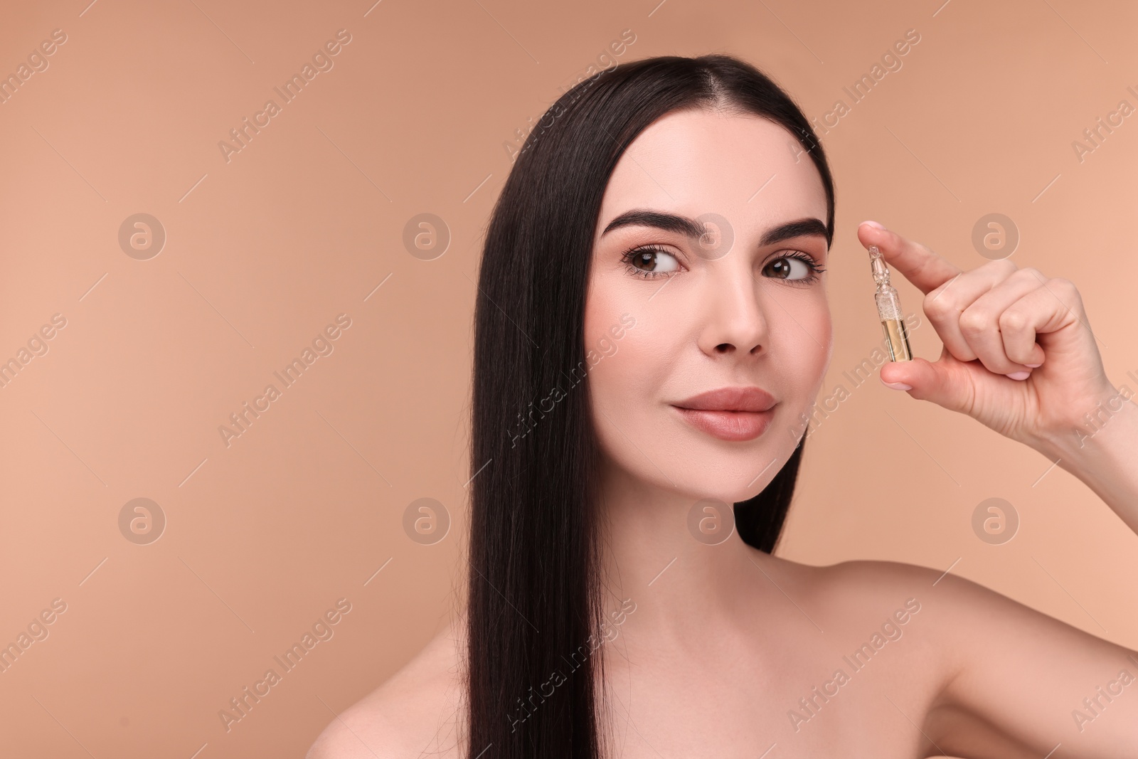 Photo of Beautiful young woman holding skincare ampoule on beige background. Space for text