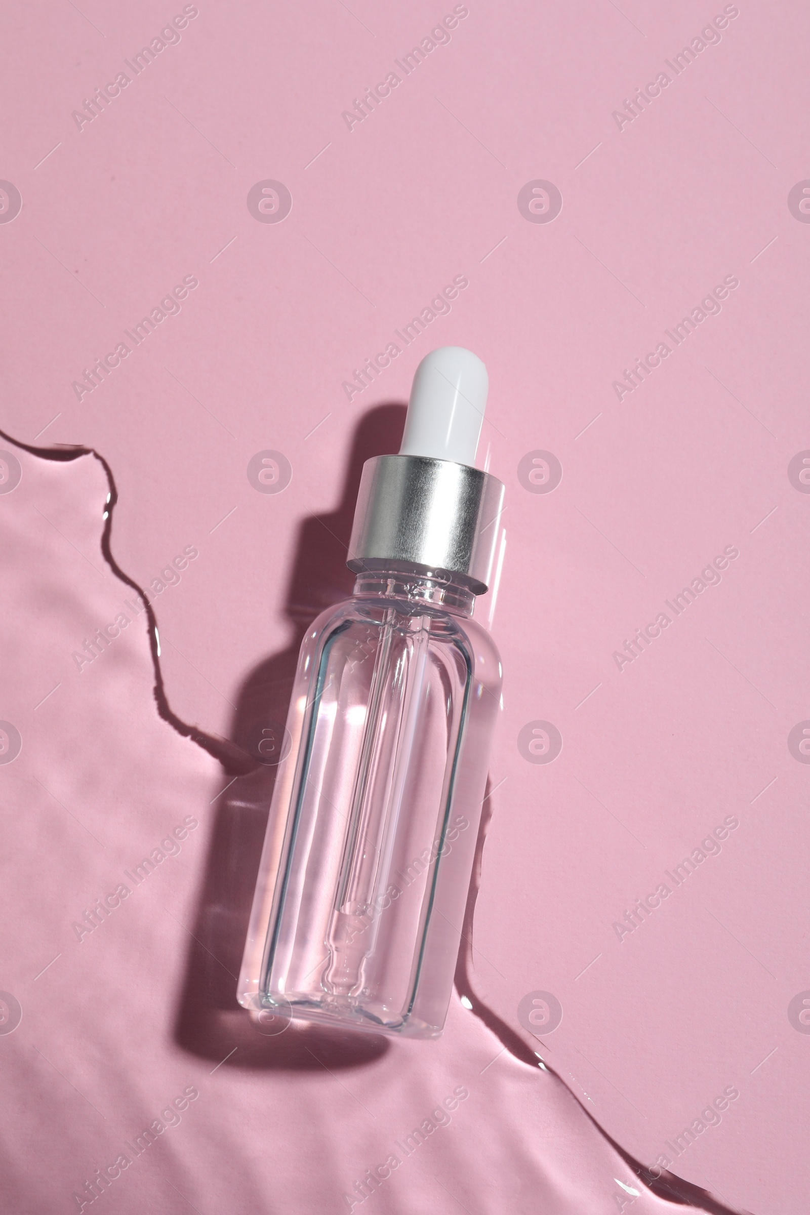 Photo of Bottle of cosmetic oil in water on pink background, top view