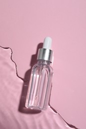 Photo of Bottle of cosmetic oil in water on pink background, top view