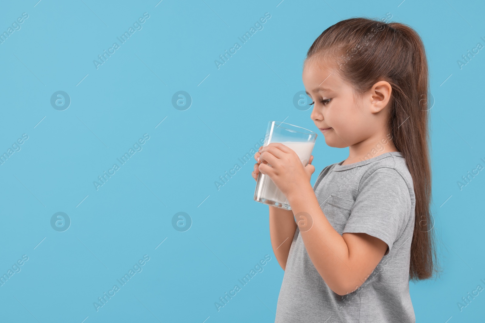 Photo of Cute girl with glass of fresh milk on light blue background, space for text