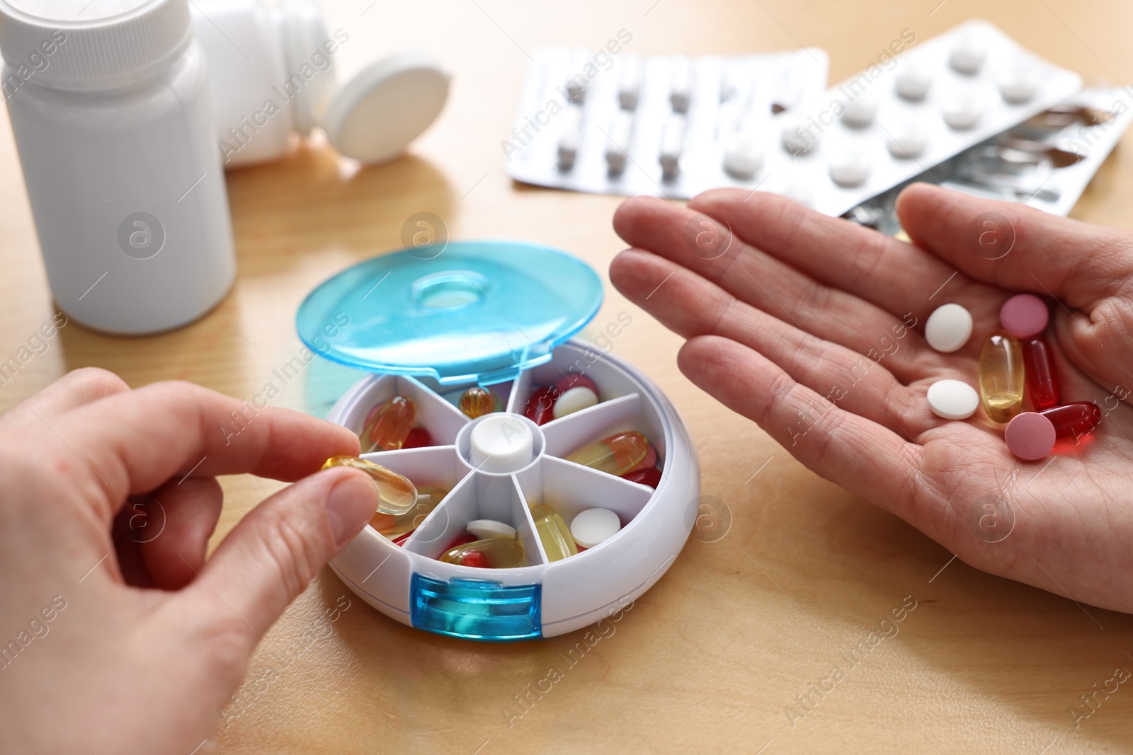 Photo of Woman with pills and organizer at light wooden table, closeup