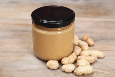 Tasty nut paste in jar and peanuts on wooden table, closeup