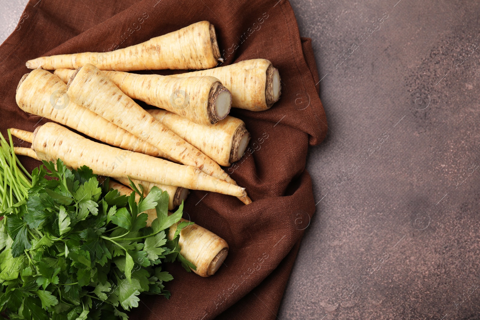 Photo of Whole raw parsley roots and bunch of fresh herb on brown table, flat lay. Space for text