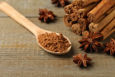 Photo of Spoon with cinnamon powder, sticks and star anise on wooden table, closeup