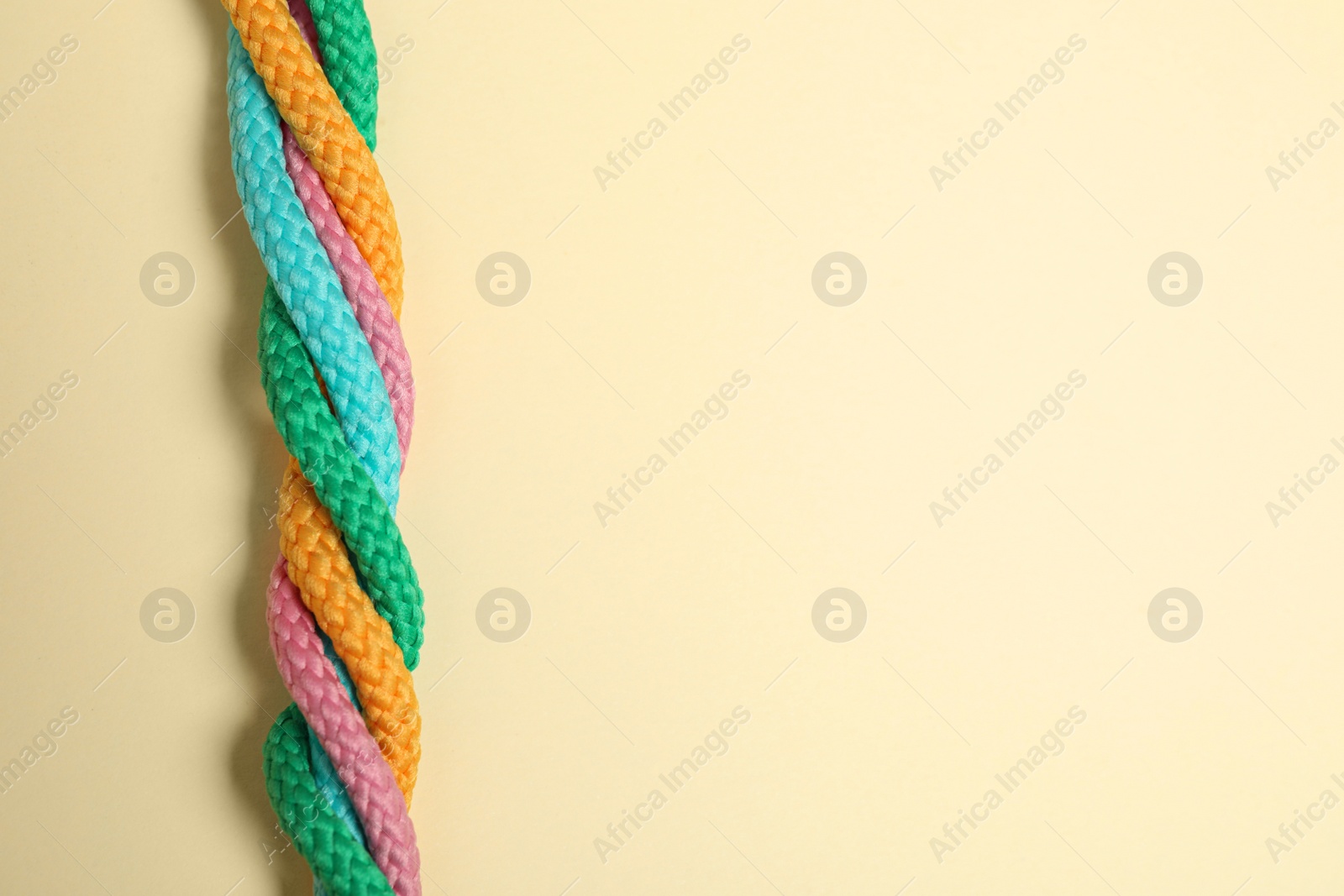 Photo of Top view of twisted colorful ropes on beige background, space for text. Unity concept