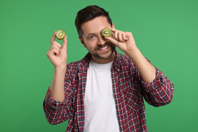 Photo of Man holding halves of kiwi on green background