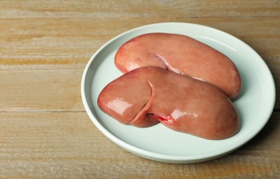 Photo of Plate with fresh raw pork kidneys on wooden table