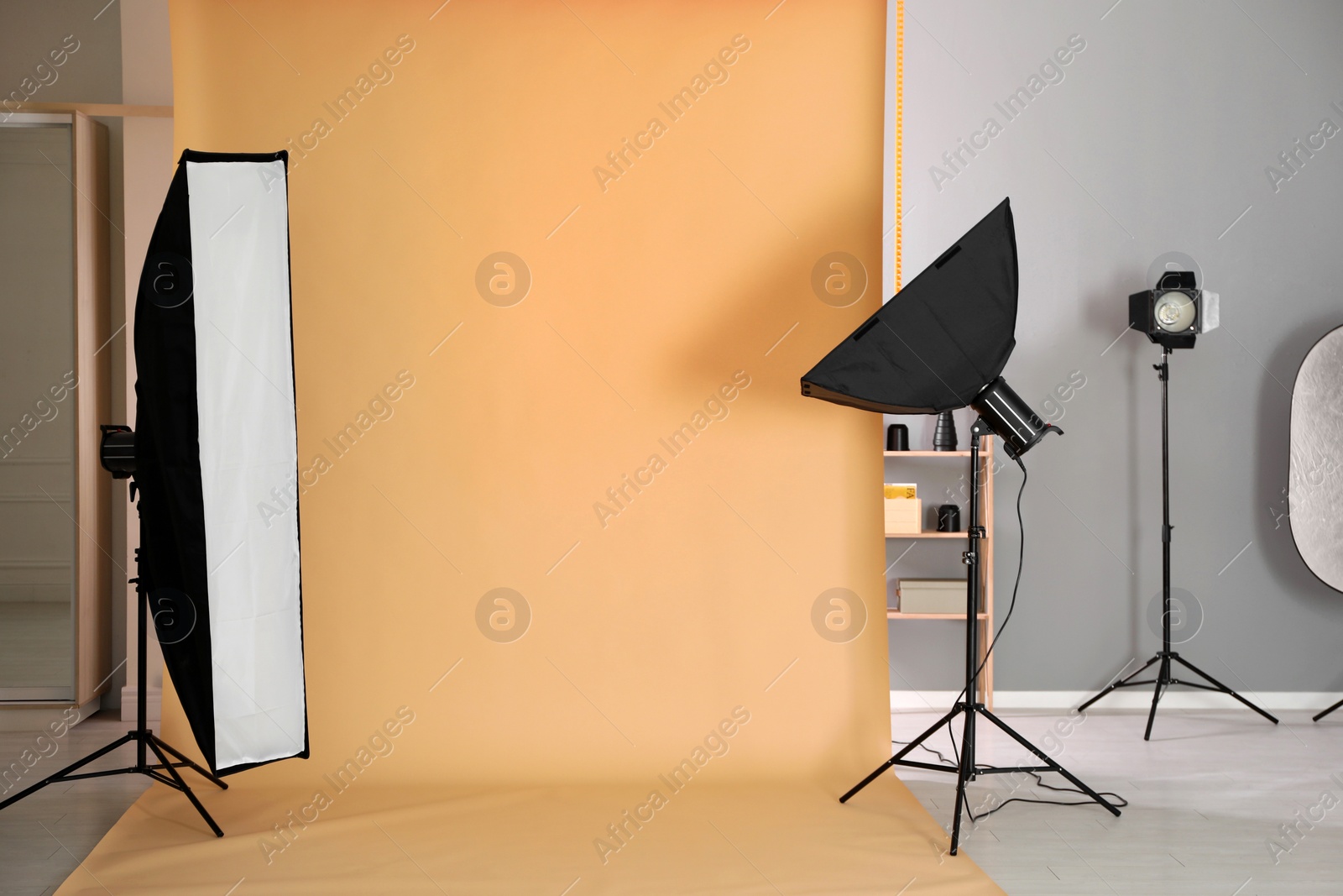 Photo of Pale orange photo background and professional lighting equipment in modern studio