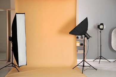 Photo of Pale orange photo background and professional lighting equipment in modern studio