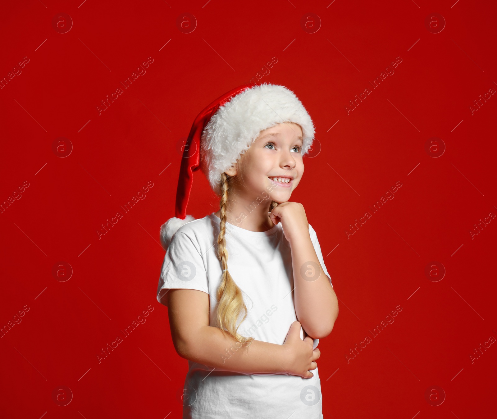 Photo of Cute little child wearing Santa hat on red background. Christmas holiday