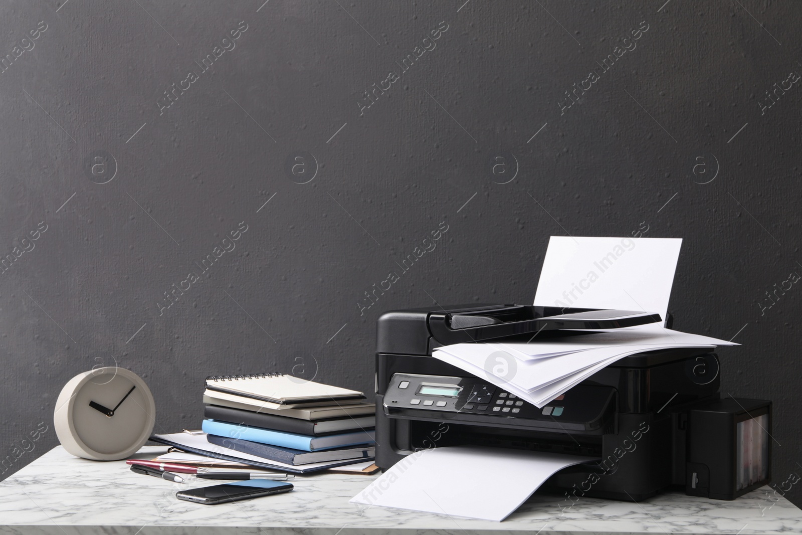 Photo of Modern printer with paper and office supplies on white marble table