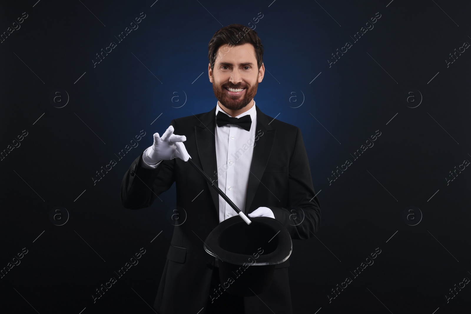 Photo of Happy magician showing magic trick with top hat on dark blue background