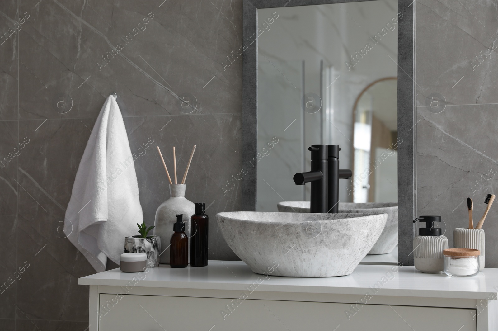 Photo of Stone vessel sink with faucet and toiletries on white countertop in bathroom