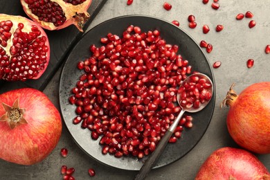 Photo of Ripe juicy pomegranates with grains on grey textured table, flat lay