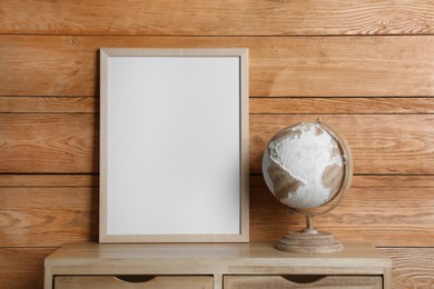 Photo of Empty frame with globe on table near wooden wall. Mockup for design