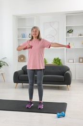 Photo of Senior woman exercising with dumbbells on mat at home. Sports equipment