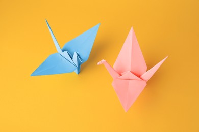 Photo of Origami art. Beautiful light blue and pale pink paper cranes on orange background