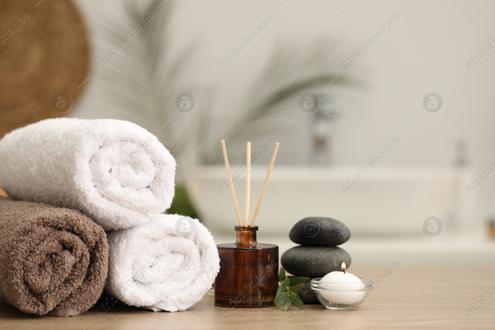 Photo of Spa composition. Rolled towels, aroma diffuser, massage stones and burning candle on wooden table indoors. Space for text