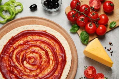 Photo of Flat lay composition with pizza crust and ingredients on grey table, closeup