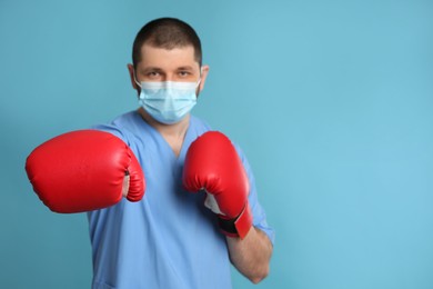 Photo of Doctor with protective mask and boxing gloves on light blue background, space for text. Strong immunity concept