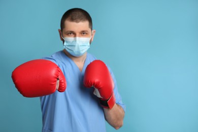 Doctor with protective mask and boxing gloves on light blue background, space for text. Strong immunity concept