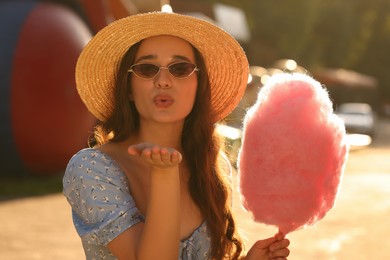 Beautiful young woman with cotton candy blowing kiss outdoors on sunny day