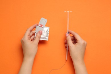 Photo of Woman with condom, contraceptive pills and intrauterine device on orange background, top view. Choosing birth control method