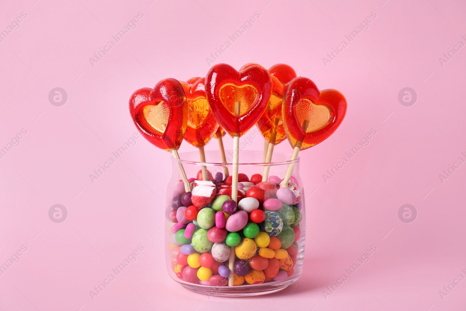Photo of Glass jar with different candies on pink background