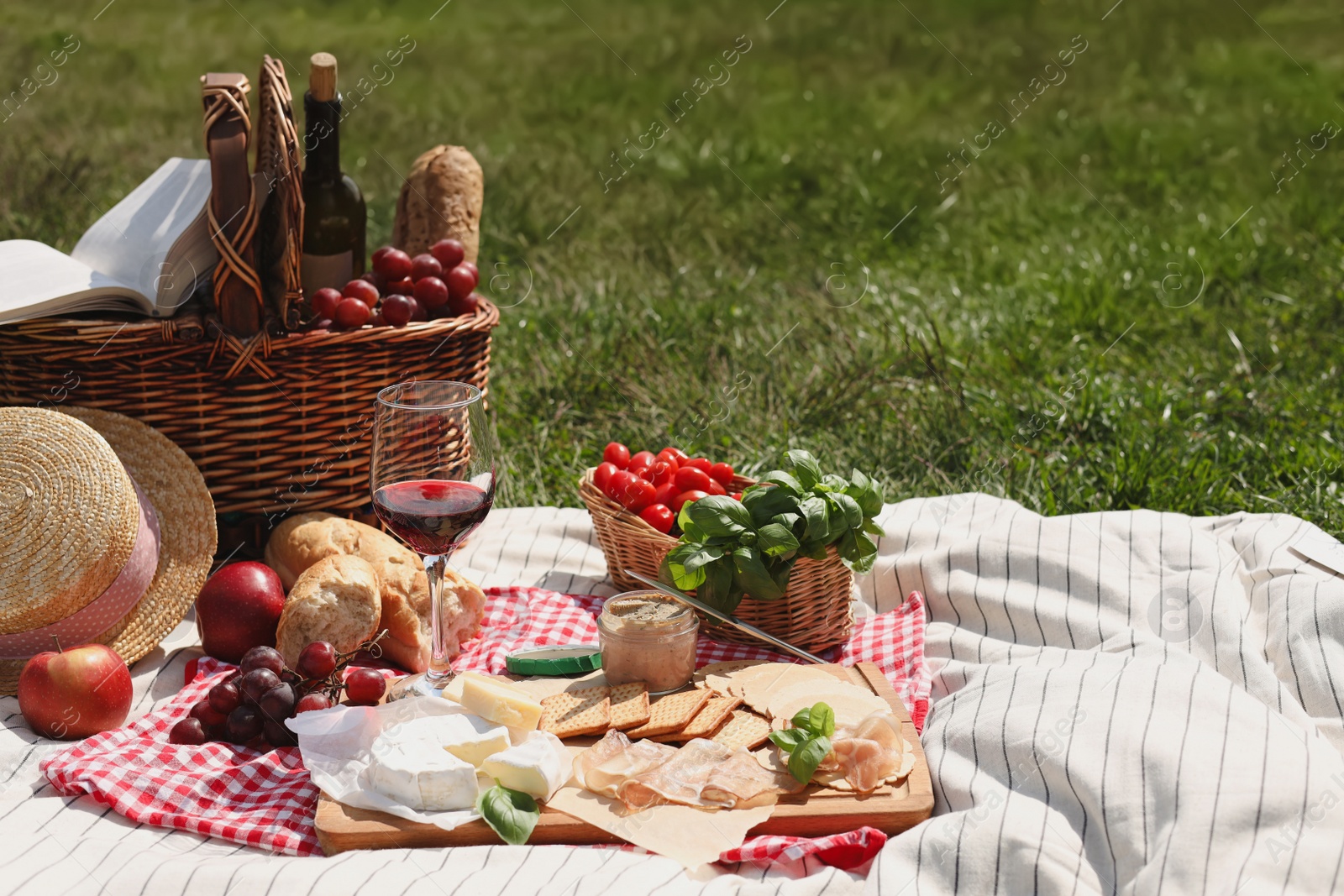 Photo of Blanket with picnic basket and different products on green grass