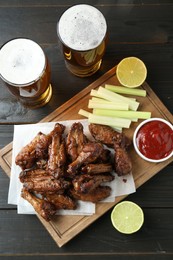 Photo of Delicious chicken wings served with beer on black wooden table, flat lay