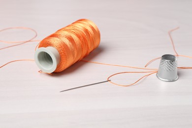 Photo of Sewing needle, spool of threads and thimble at light wooden table , closeup