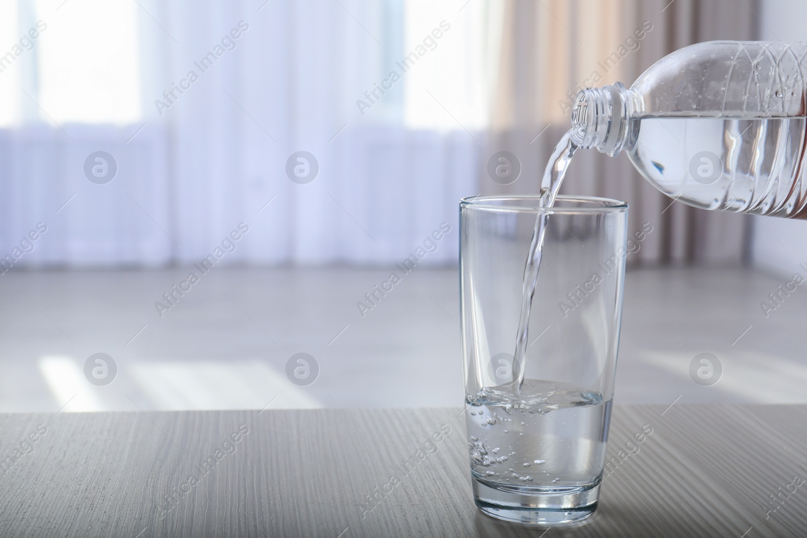 Photo of Pouring water from bottle into glass on blurred background. Space for text