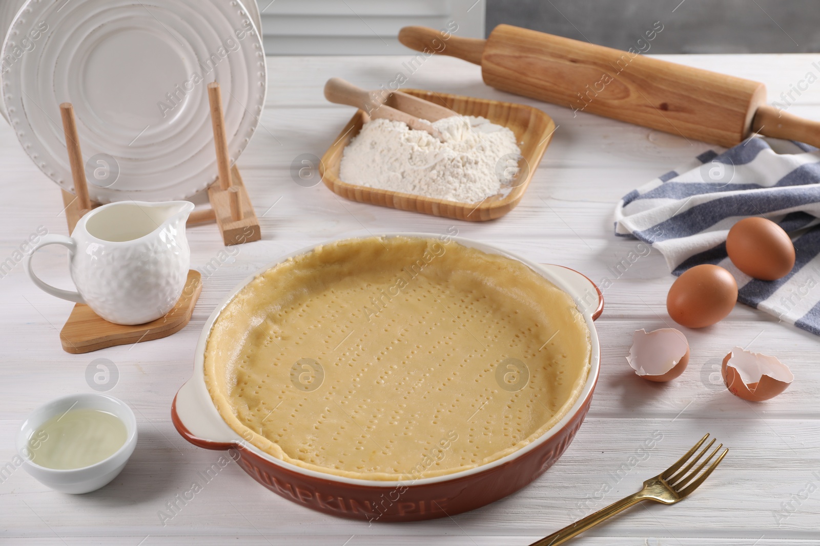 Photo of Pie tin with fresh dough, rolling pin and ingredients on white wooden table. Making quiche