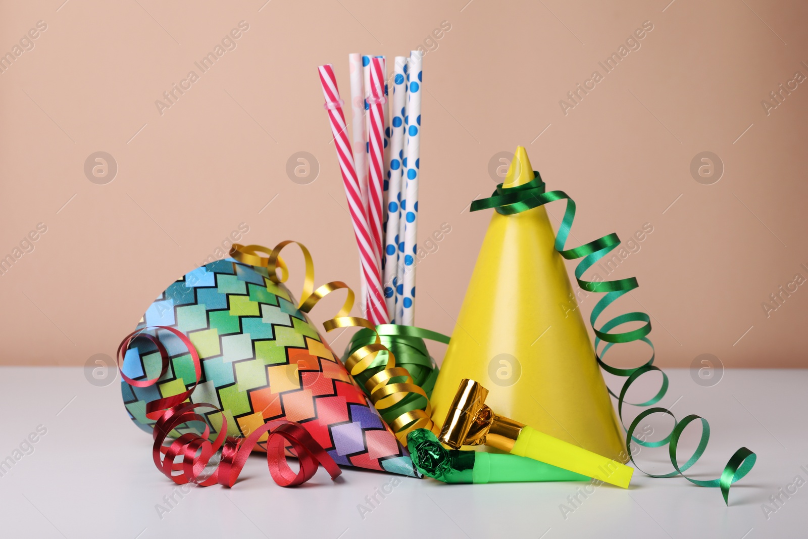 Photo of Colorful party hats, streamers and straws on white table. Birthday celebration