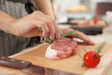Photo of Female chef preparing meat on wooden board at table, closeup
