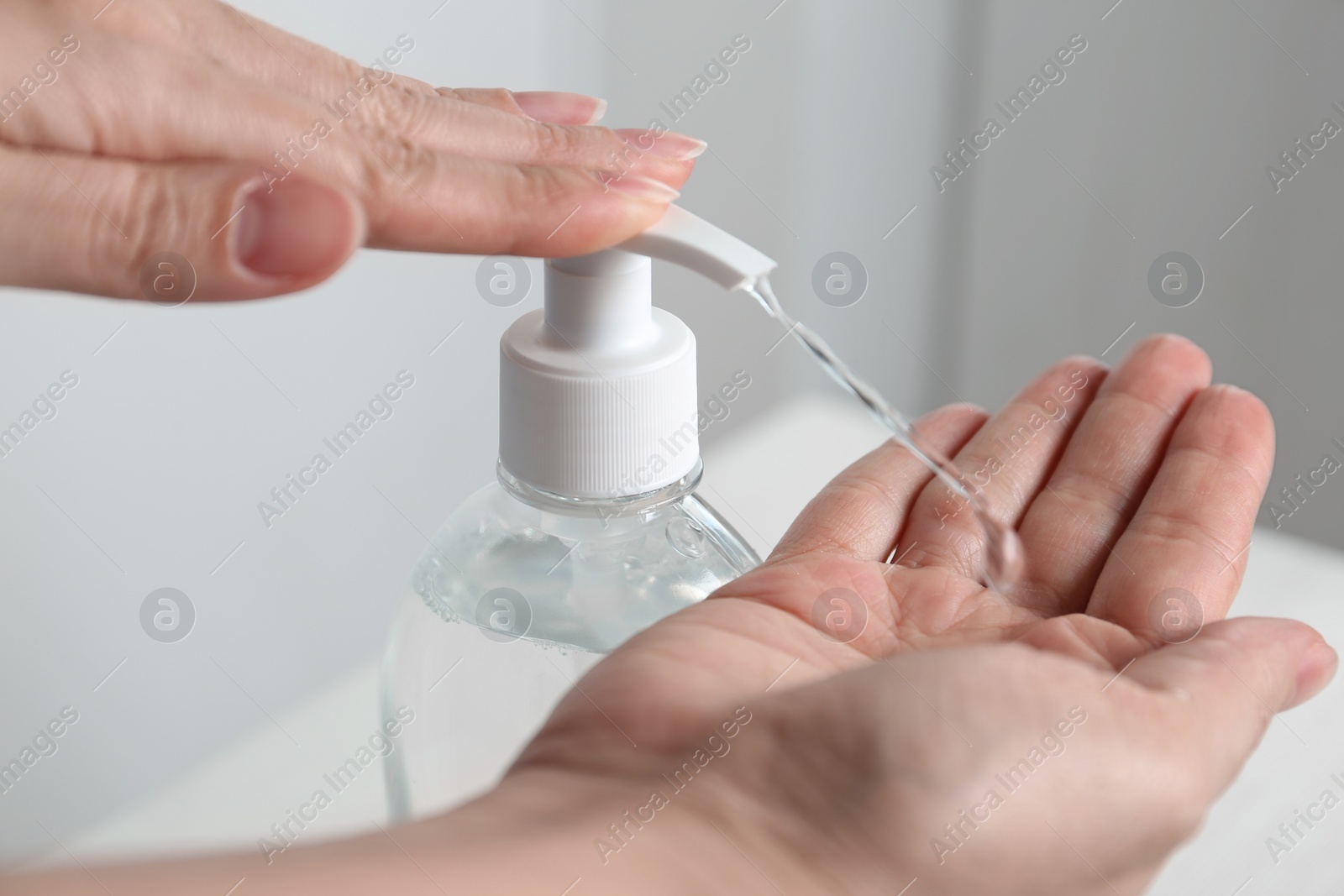 Photo of Woman applying antiseptic gel on hand indoors, closeup