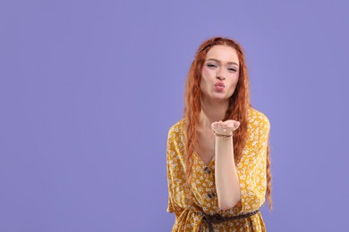 Photo of Beautiful young hippie woman blowing kiss on violet background, space for text