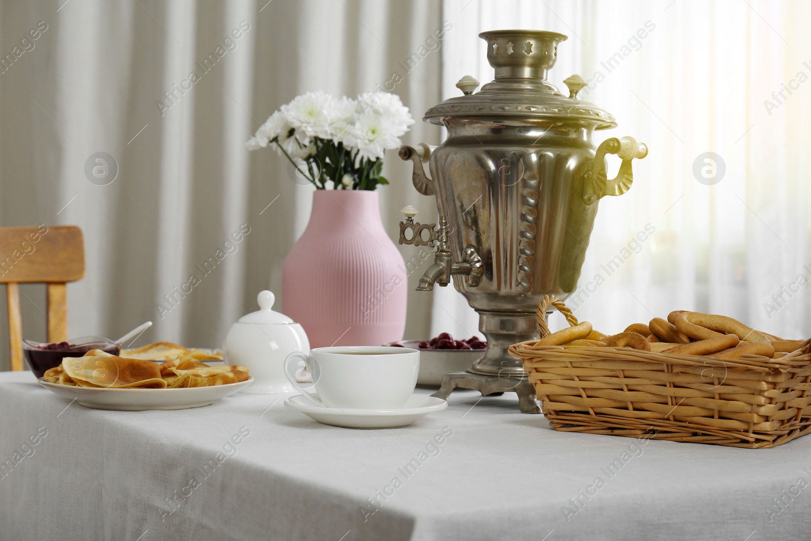 Photo of Vintage samovar, cup of hot drink and snacks served on table indoors. Traditional Russian tea ceremony