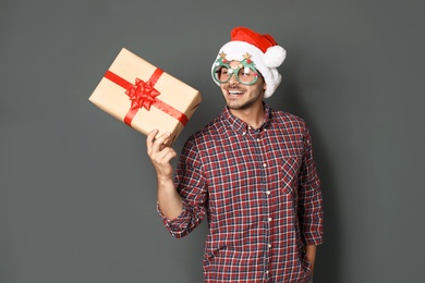 Young man with Christmas gift on grey background