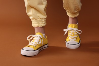 Photo of Woman wearing yellow classic old school sneakers on brown background, closeup