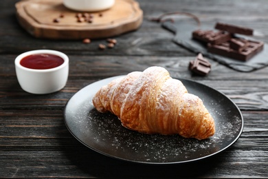 Photo of Plate with tasty croissant and powdered sugar on dark wooden table. French pastry