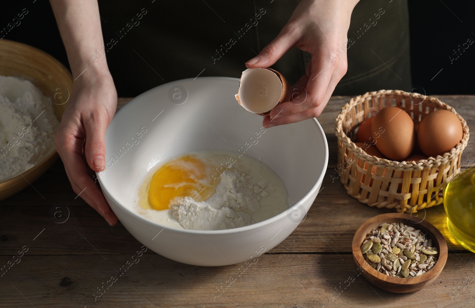 Photo of Making bread. Woman adding egg into dough at wooden table on dark background, closeup