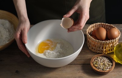 Photo of Making bread. Woman adding egg into dough at wooden table on dark background, closeup