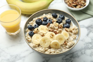 Tasty oatmeal with banana, blueberries, walnuts and milk served in bowl on white marble table