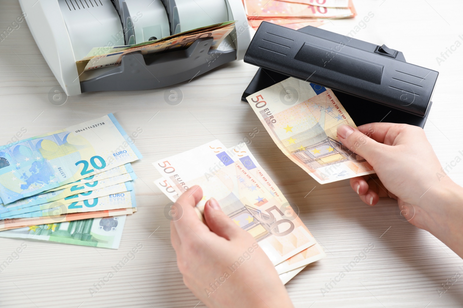 Photo of Woman checking Euro banknotes with currency detector at white wooden table, closeup. Money examination device