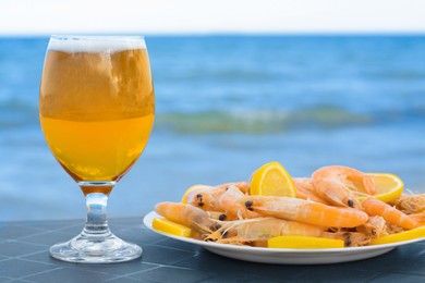 Cold beer in glass and shrimps served with lemon on beach