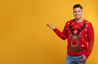 Photo of Handsome man in Christmas sweater on yellow background, space for text