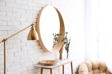 Big round mirror, table with jewelry and decor near brick wall in hallway interior