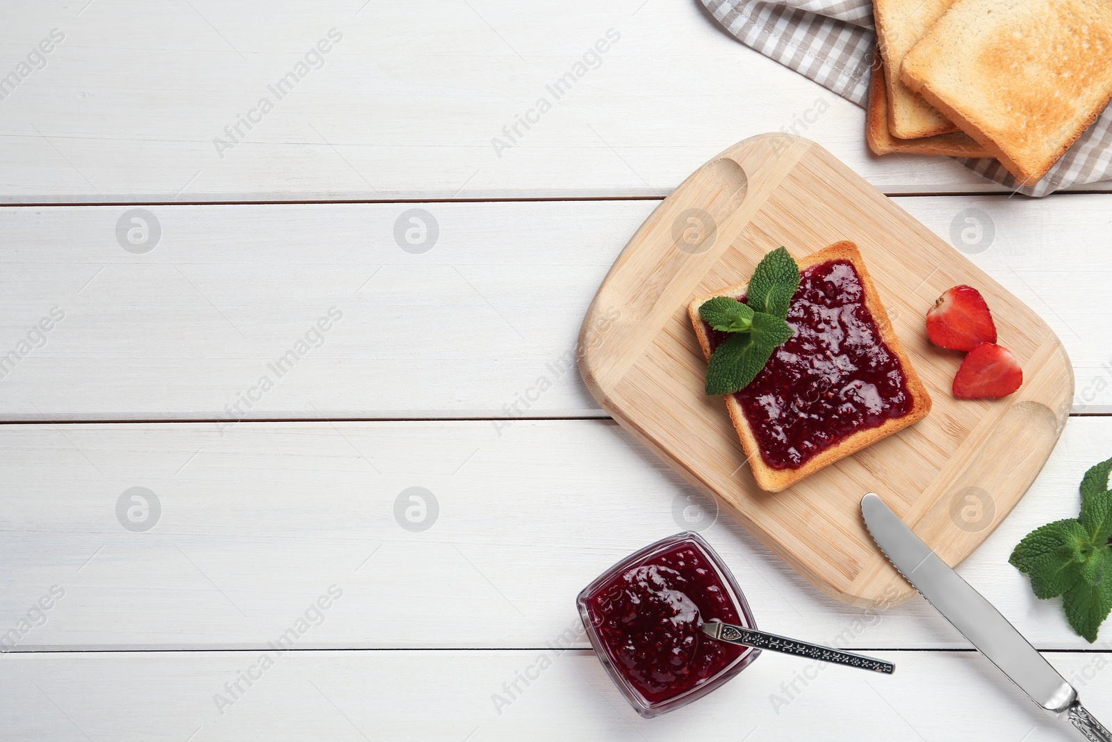 Photo of Toasts served with tasty jam, mint and strawberry on white wooden table, flat lay. Space for text